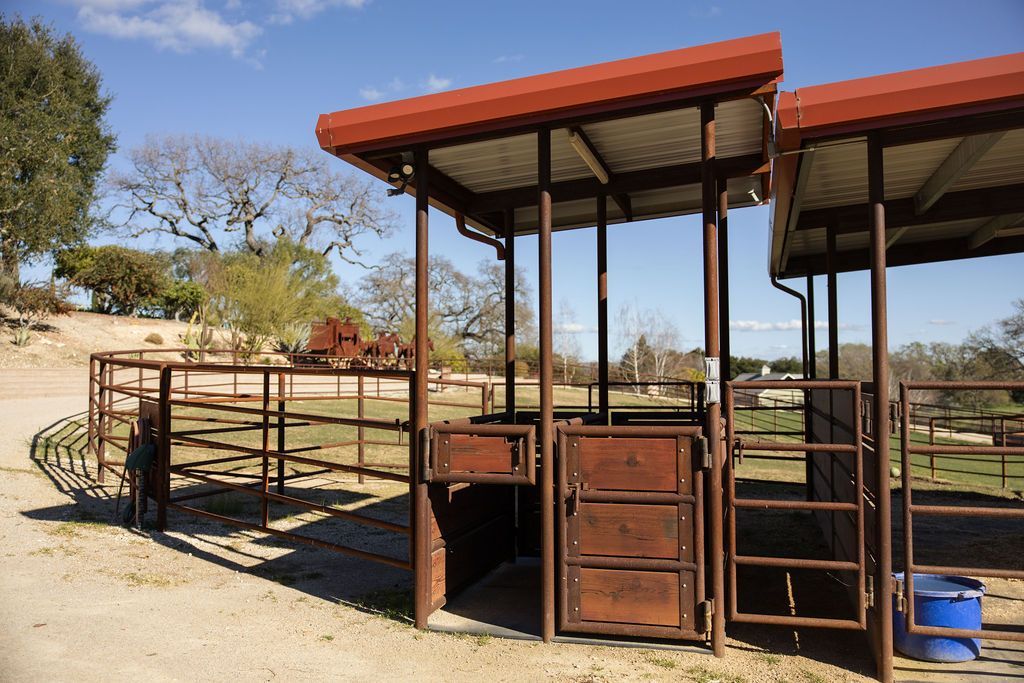 Open-sided red-roof livestock shelter and corral in a dry rural field.