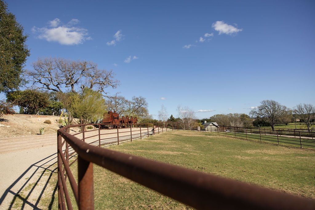 Rust-colored fence beside a grassy park path under a clear blue sky with scattered clouds.
