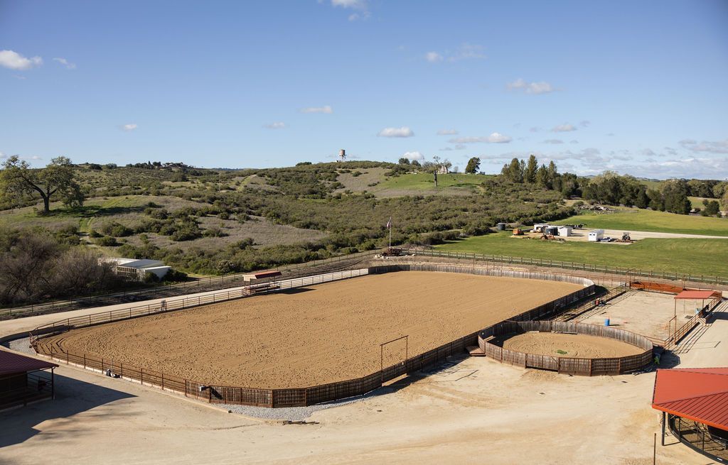 Outdoor dirt arena surrounded by stone walls and trees under a clear blue sky