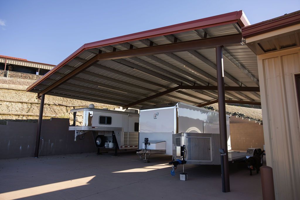 Covered outdoor carport with parked vehicles and trailers in a desert lot