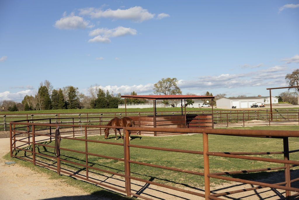 Rusty metal corral in a fenced ranch yard under a blue sky with scattered clouds