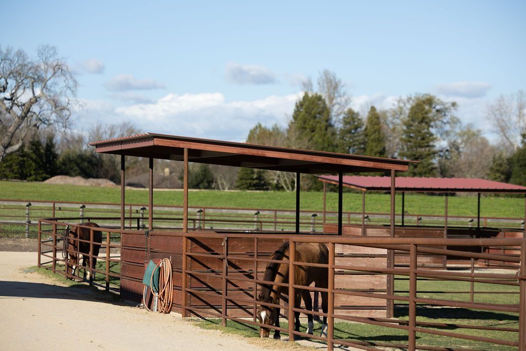 Rustic horse corral with brown fences and a metal-roofed shelter in a grassy field