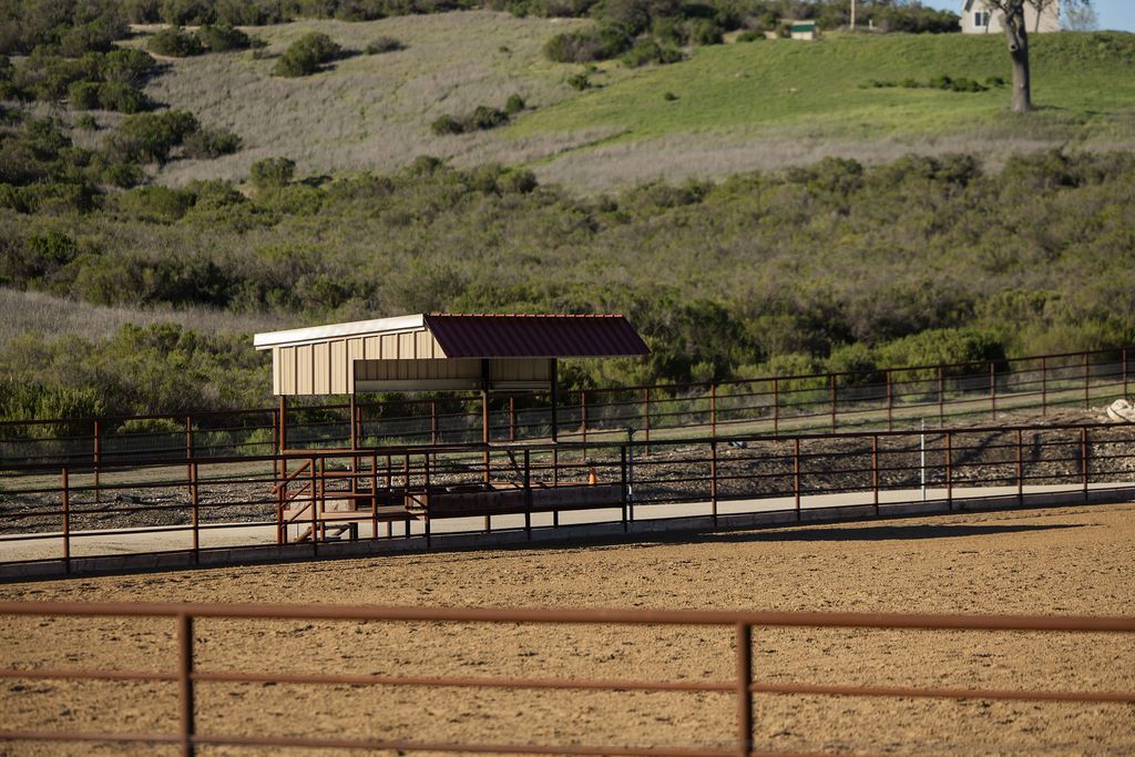 Small fenced corral with a roofed shelter in a dry grassy field, with hills in the background