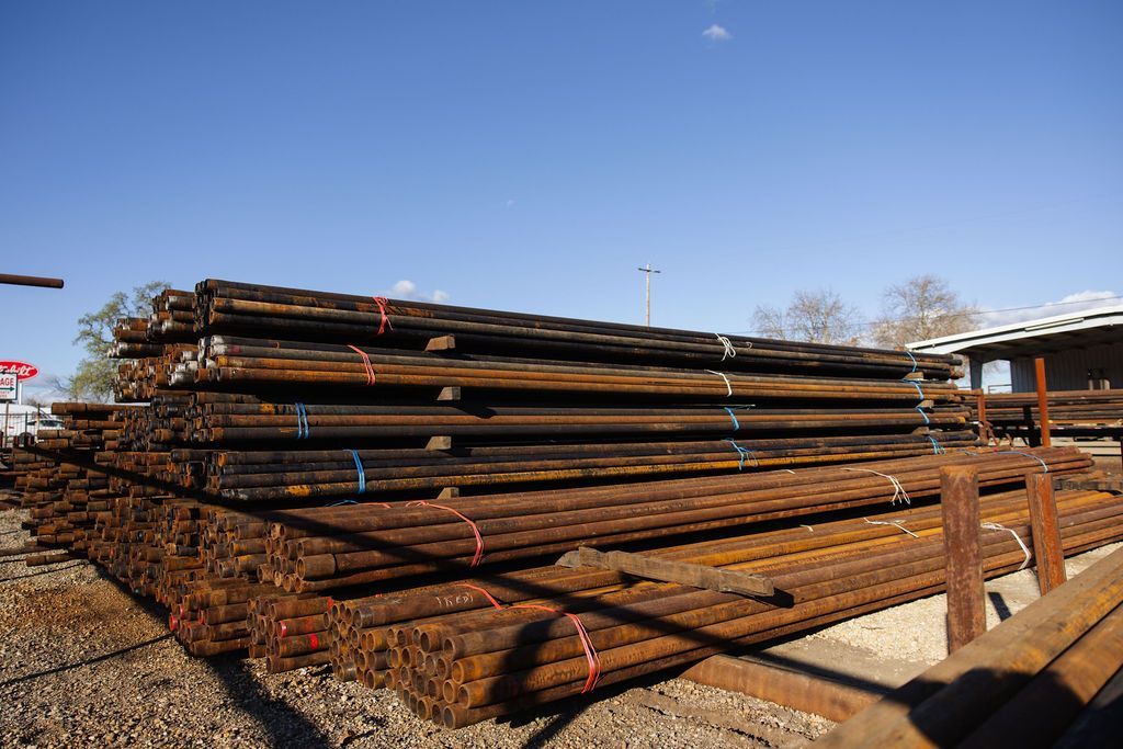 Stacked metal pipes in an outdoor yard under a clear blue sky.