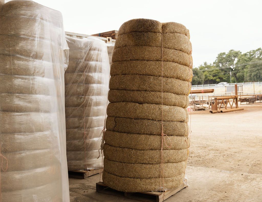 Stacked straw wattle wrapped in plastic on pallets in an outdoor yard