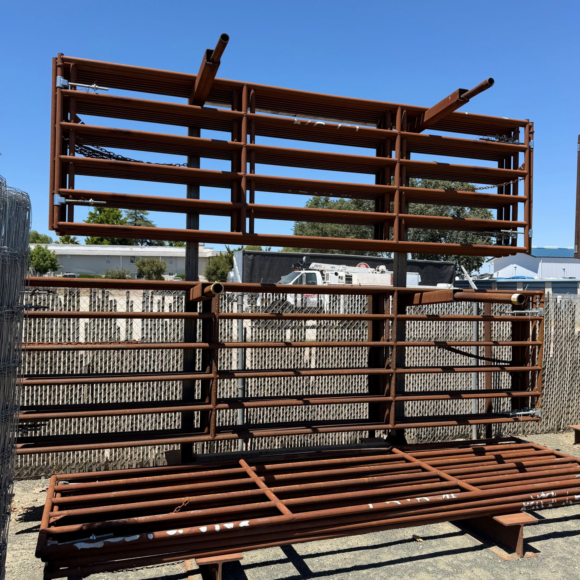 Rusty metal shelving racks stacked outdoors in a yard against a fence under a blue sky