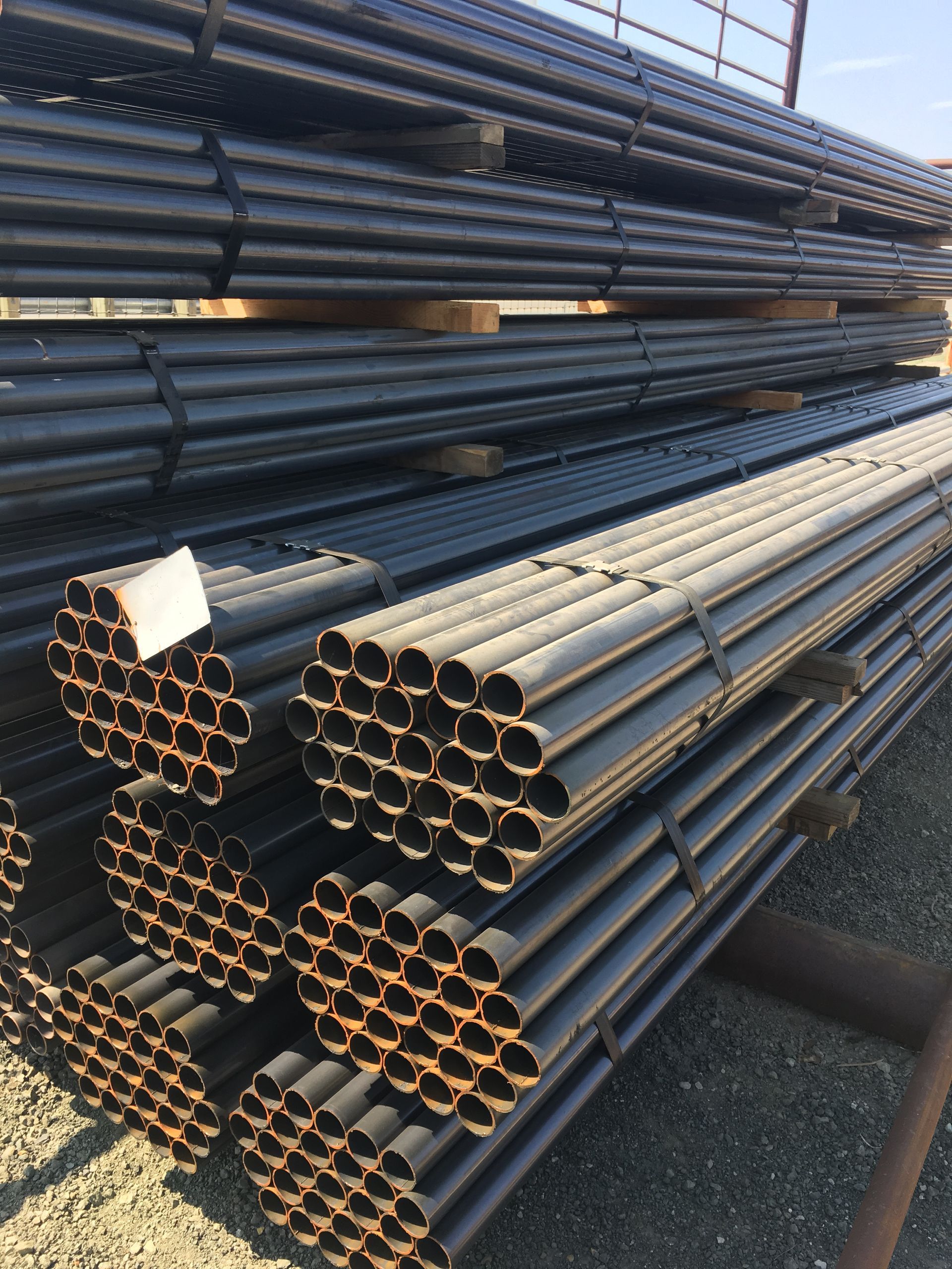 Stacks of black steel pipes with gold ends piled in a storage yard