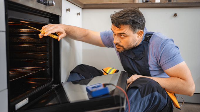 “Repair technician inspecting the inside of a built-in oven with tools nearby during an appliance repair service in Taylorsville, UT”