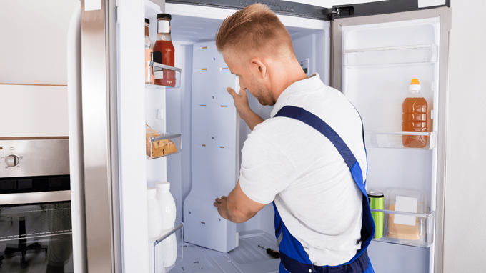 “Technician inspecting the inside of a refrigerator with shelves and food items during an appliance repair service in Taylorsville, UT”