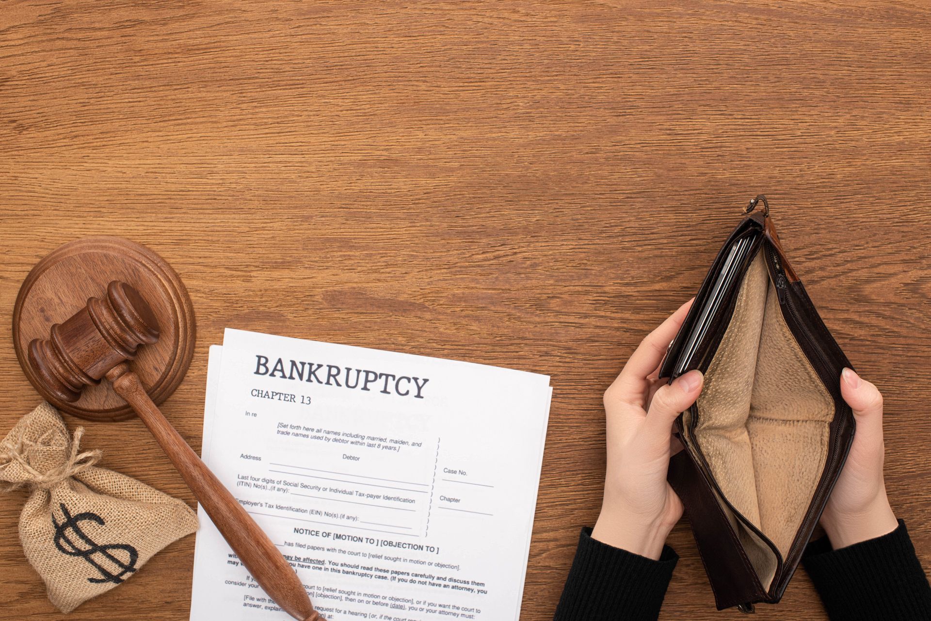 Hands holding an empty wallet beside a bankruptcy form and a wooden gavel on a table