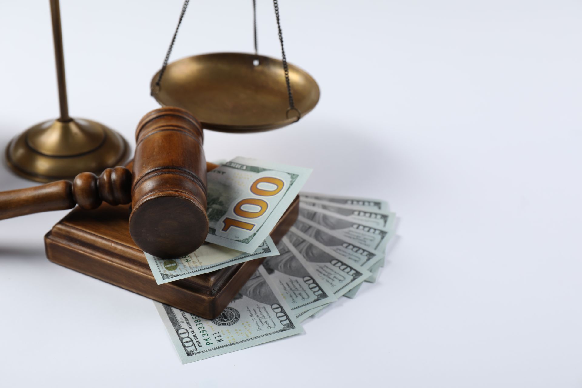 Gavel, scales of justice, and US $100 bills on a white surface, symbolizing legal and financial concepts.