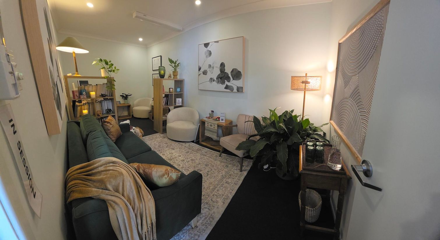 Small cozy living room with green sofa, armchair, bookshelf, rug, and wall art.