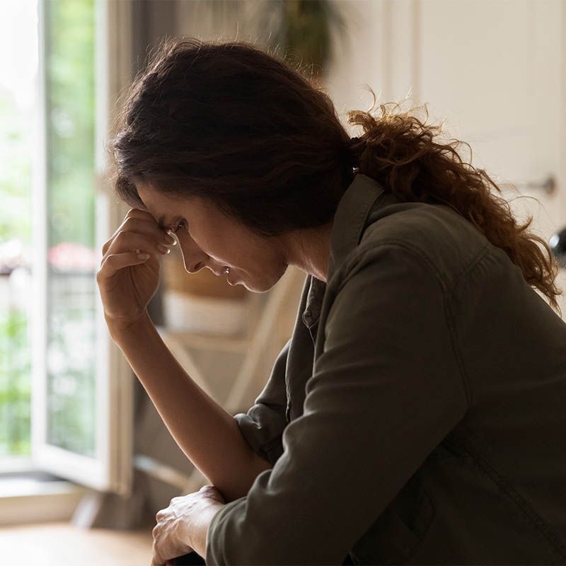 Person sitting by a window, head in hand, looking down in a thoughtful pose.