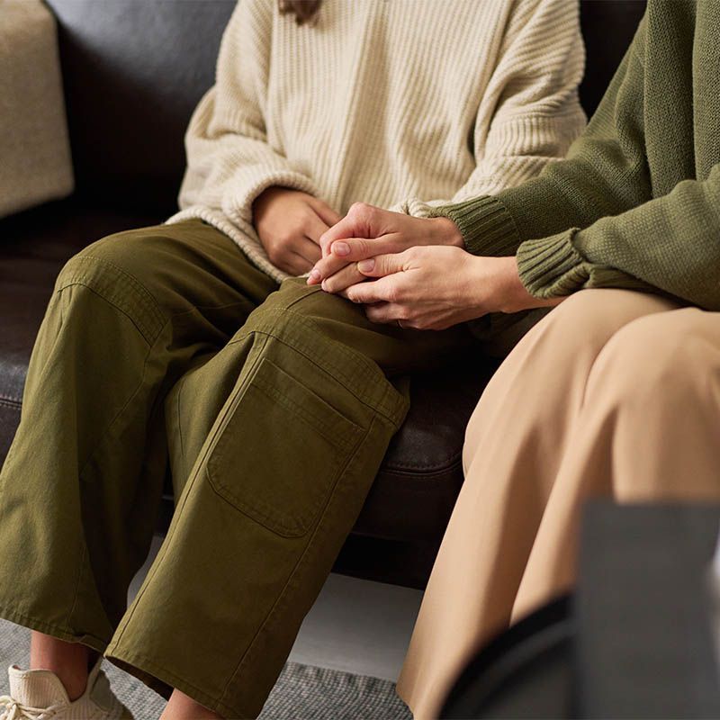 Two people sitting on a couch, holding hands, in cozy neutral-toned clothes