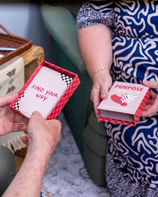 Hands holding small pink gift boxes labeled “Find Your Why” and “Purpose” at a gathering