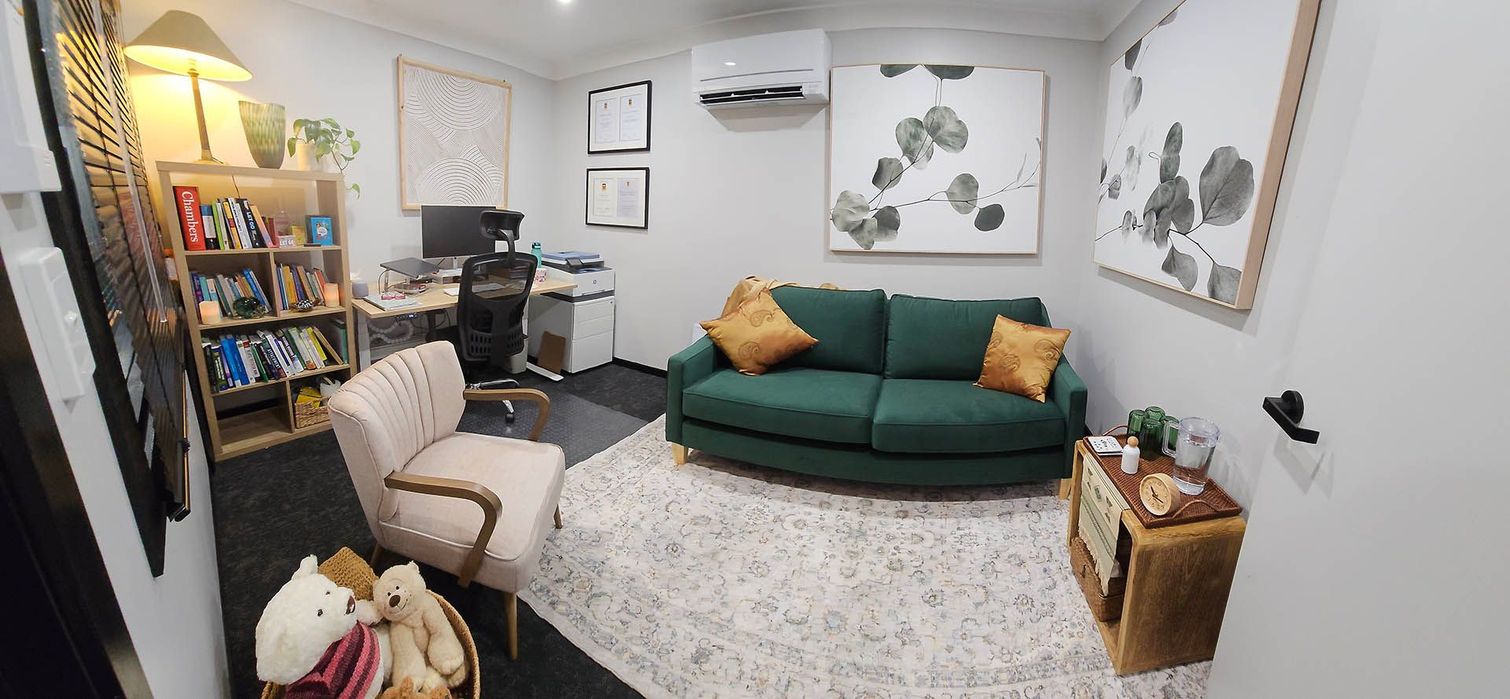 Small cozy living room with green sofa, armchair, bookshelf, rug, and wall art.