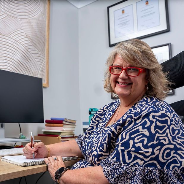 Smiling woman with red glasses writing at a desk in a framed-office setting