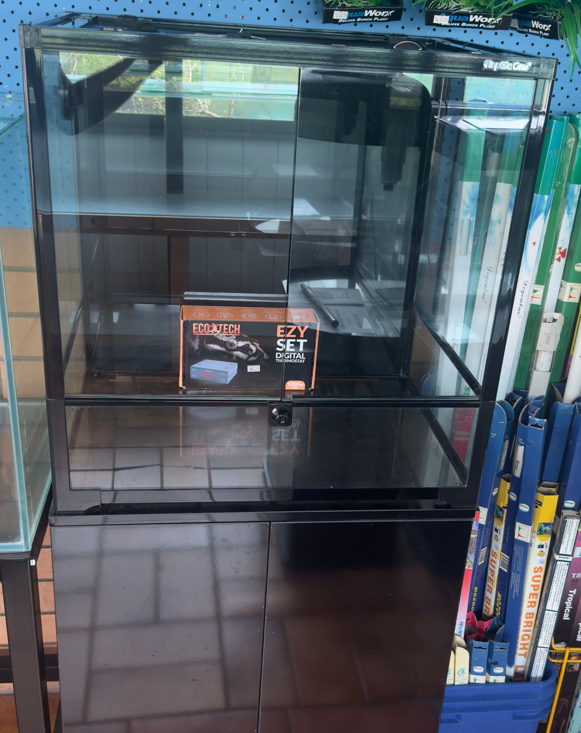 Black reptile enclosure with cabinet base; a box of accessories sits inside.