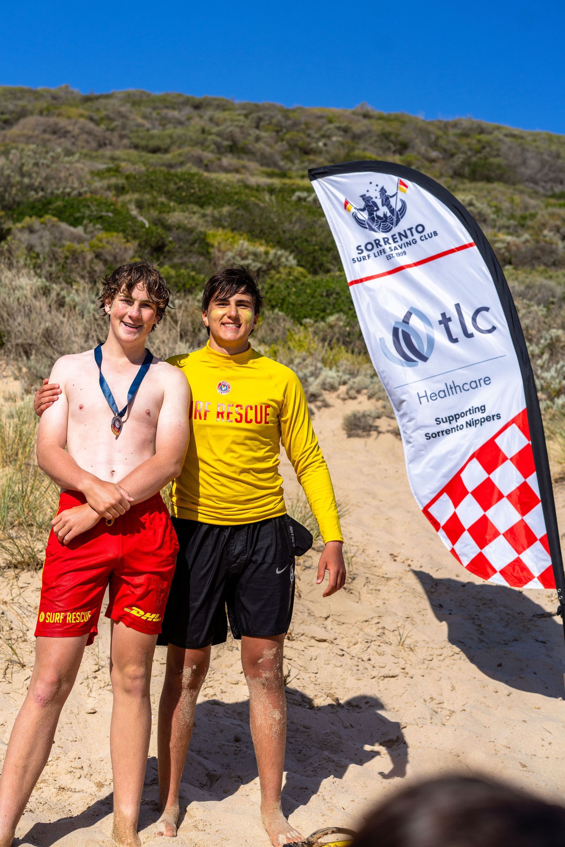 Two Sorrento lifesavers beside the TLC Healthcare Supporting Sorrento Nippers flag