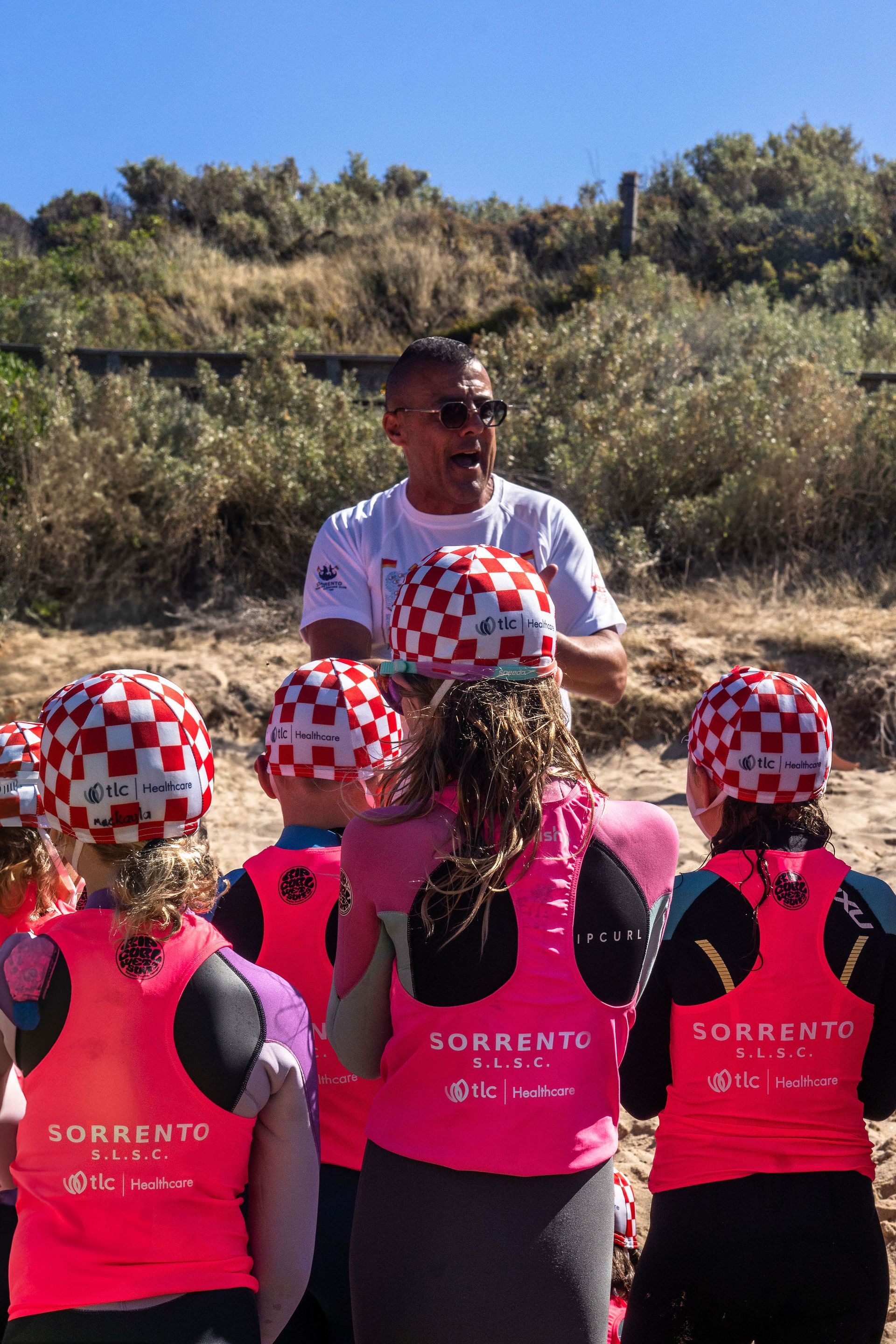 Lou talking with a group of Sorrento Nippers in TLC Healthcare rash vests on the beach
