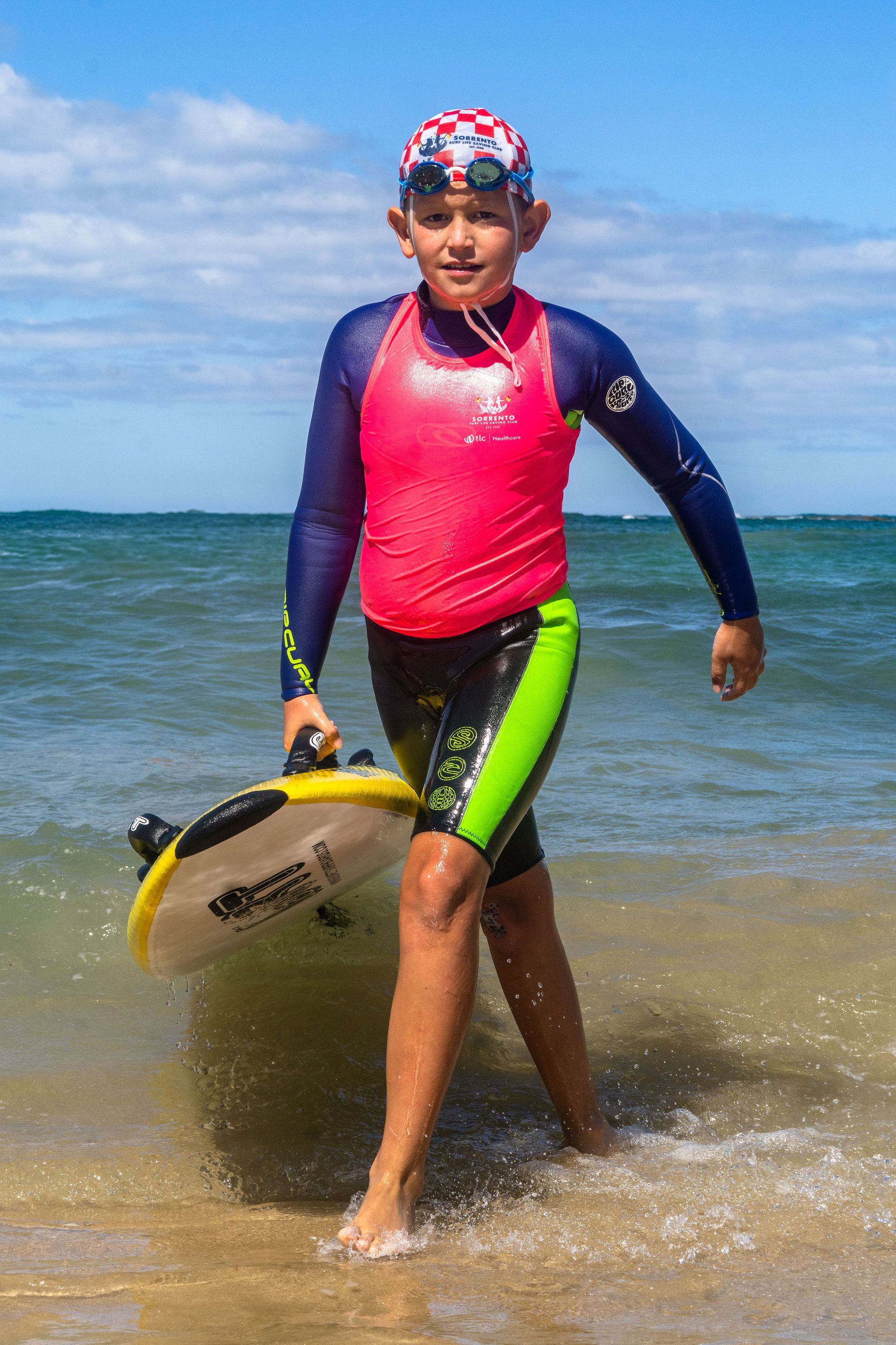 Sorrento Nipper in a pink vest carrying a bodyboard out of the water