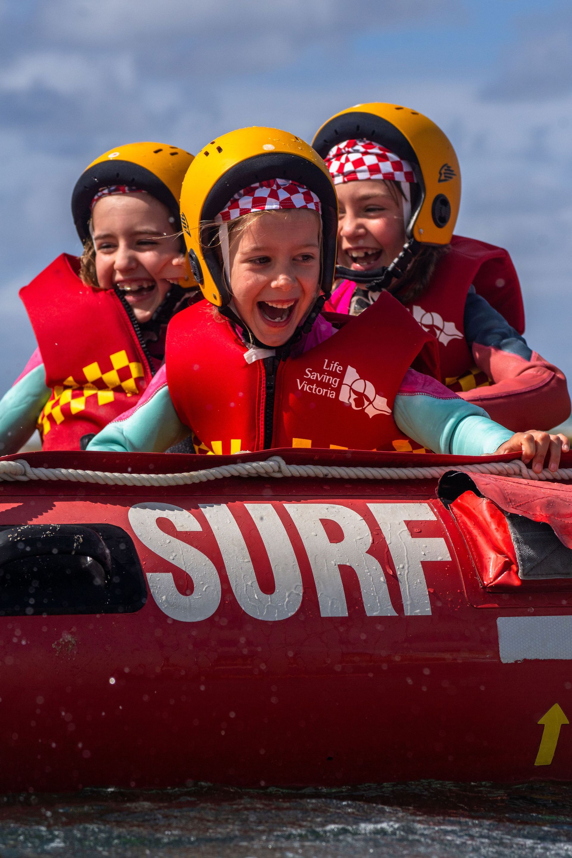 Three smiling Sorrento Nippers in helmets and life jackets riding in an IRB