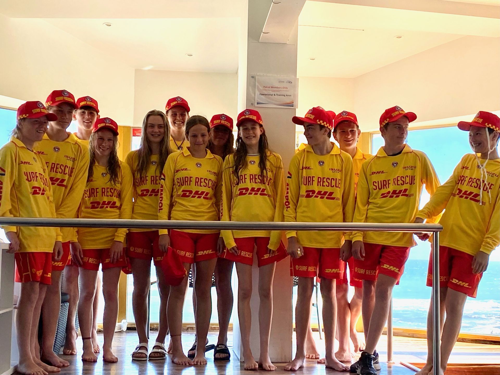 Group of lifeguards in red and yellow uniforms standing by water.