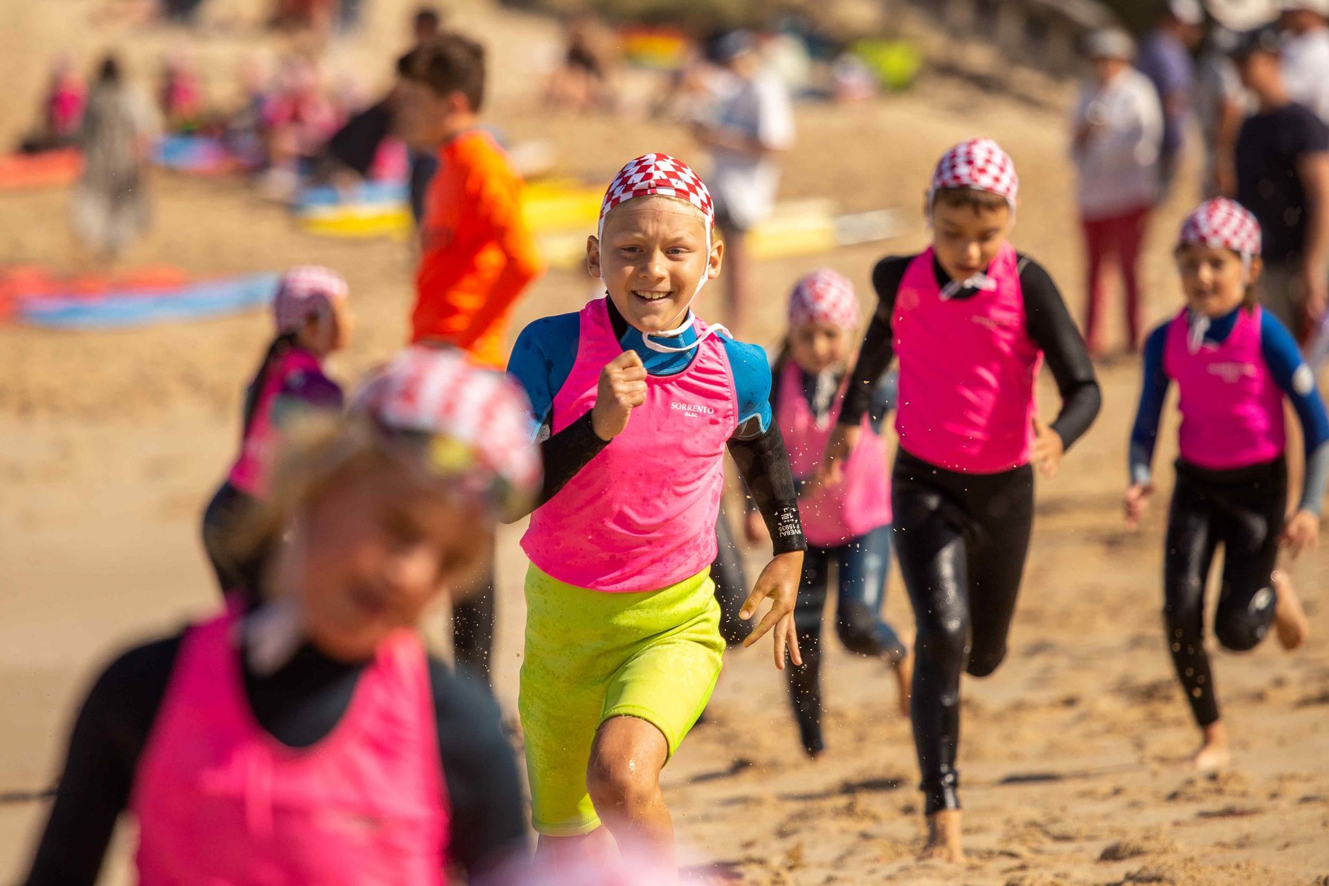 Sorrento SLSC Nippers running up the beach in pink rash vests and red-and-white caps