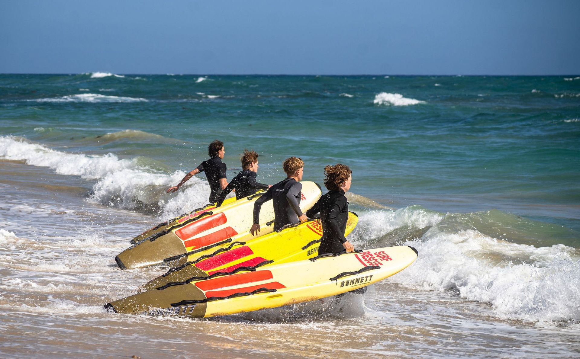 A line of members paddling rescue boards through breaking surf.