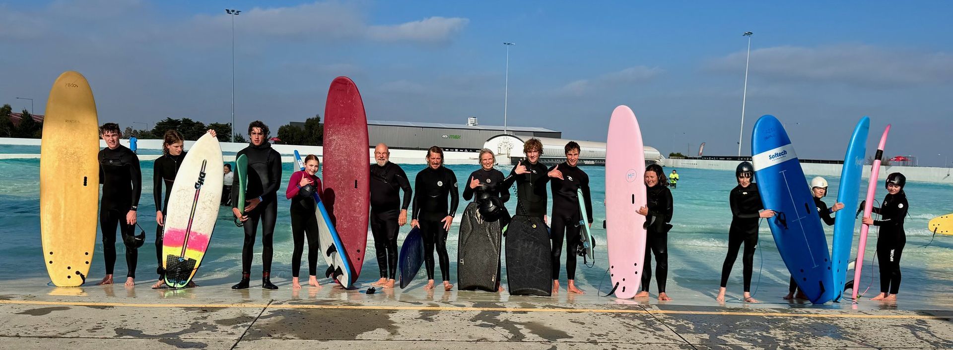 Youth members lined up holding surfboards at the URBNSURF wave pool.