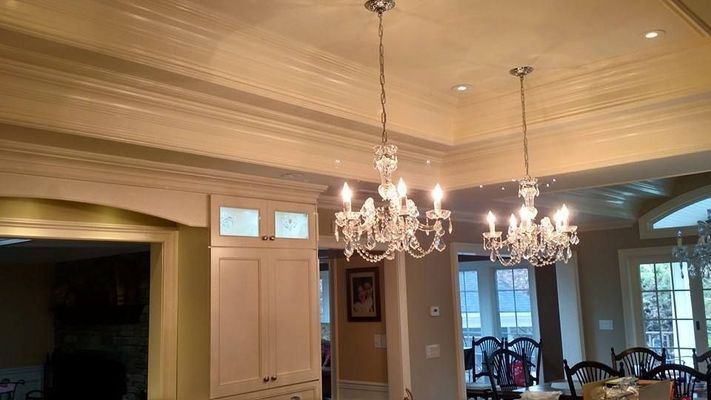 Two crystal chandeliers hang from a coffered ceiling in a well-lit room with white cabinetry.