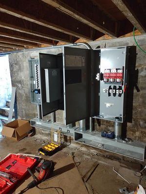 Electrical panels mounted on metal stands in a basement with tools scattered on the floor.
