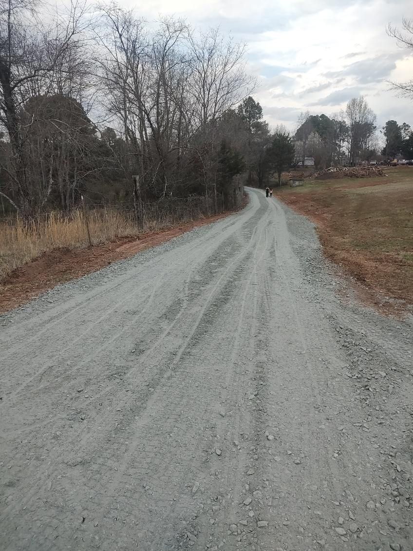 Gravel road winding through leafless trees and open fields under a cloudy sky