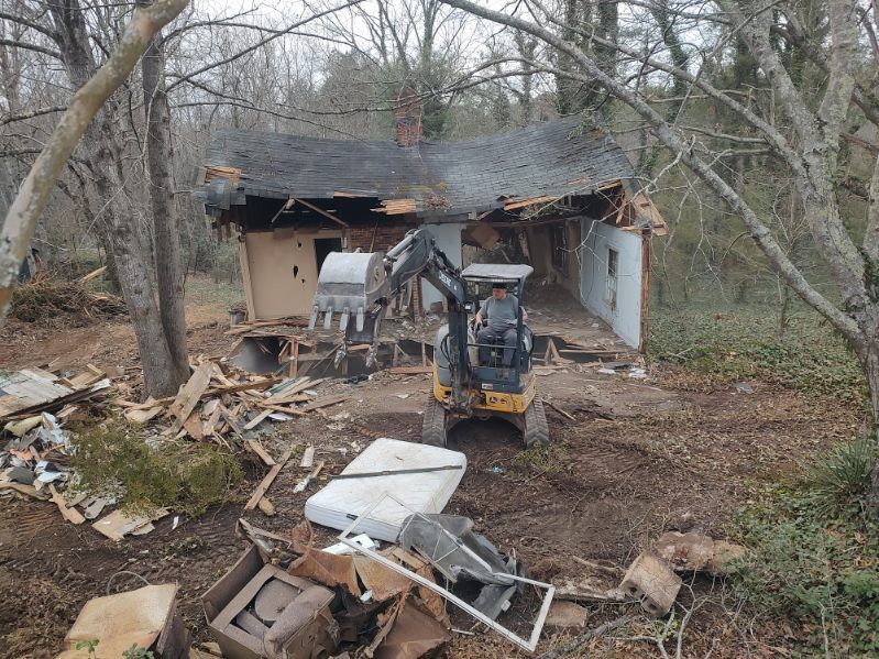 Demolished shed with excavator amid debris in a wooded yard