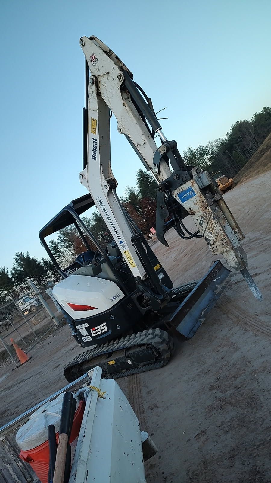 Excavator parked on a dirt lot beside a construction vehicle, under a clear sky.