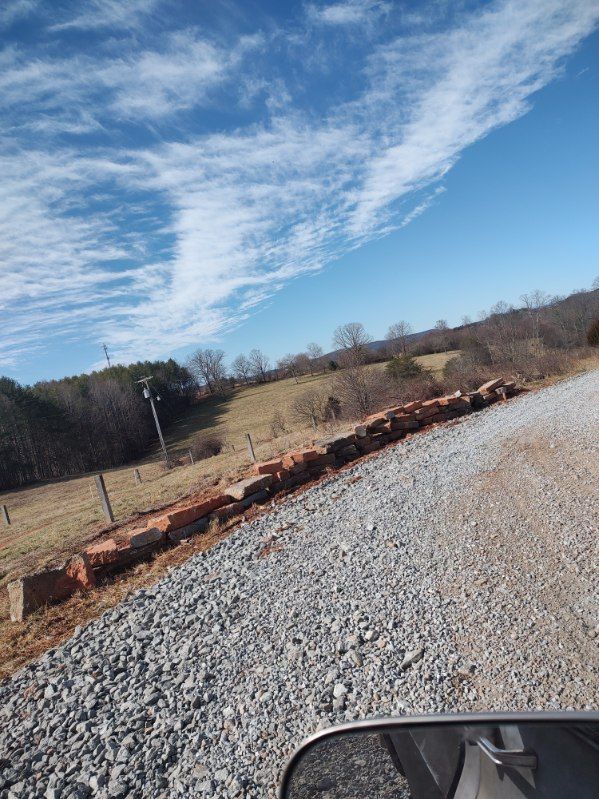 Gravel driveway beside a low brick border and bare hillside under a blue sky with wispy clouds
