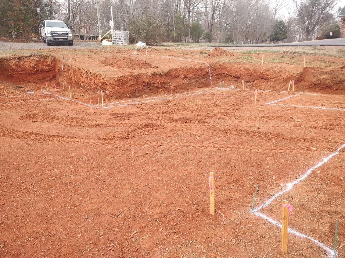 Construction site with red dirt excavation marked by white lines and stakes, with a white truck in the background