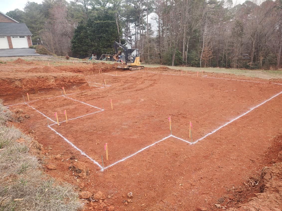 Marked excavation site with white outline in red dirt near trees and a house