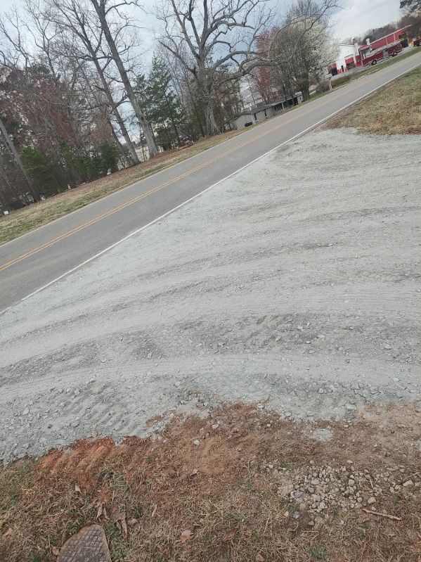 Gravel driveway beside a road, with bare trees and overcast sky in the background.