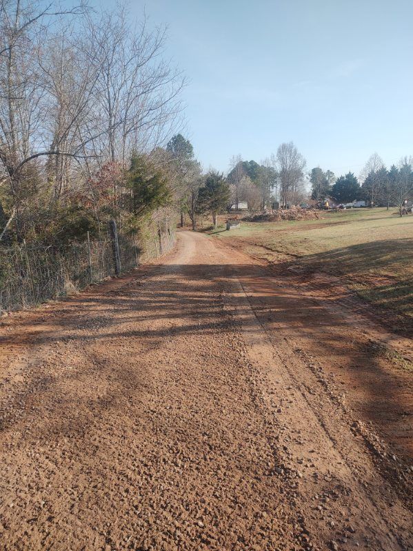 Gravel road curving through a rural field with leafless trees and long shadows on a clear day