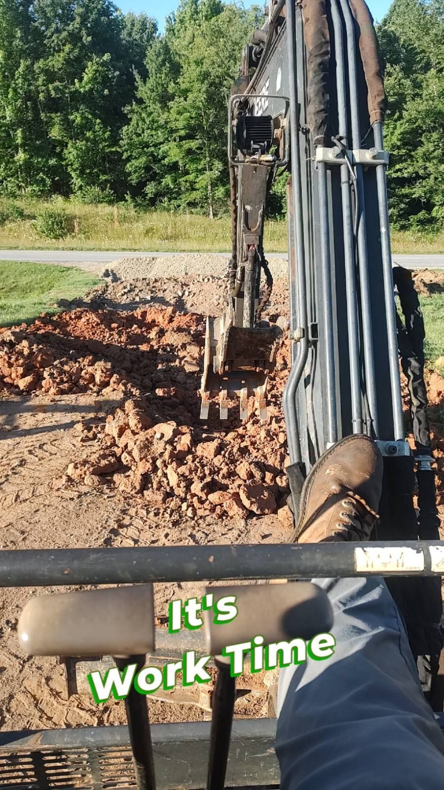 Excavator digging red dirt at a roadside site, with “It’s Work Time” text overlay.