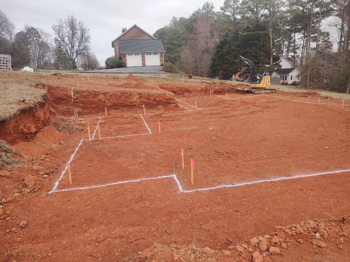 Marked red dirt lot with white foundation outlines and a house in the background