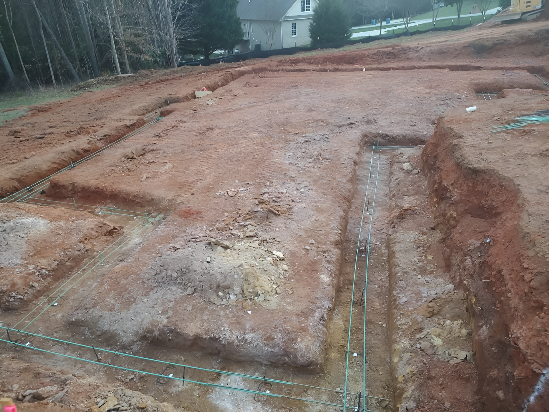 Excavated construction site with dirt trenches, graded soil, and a house in the background