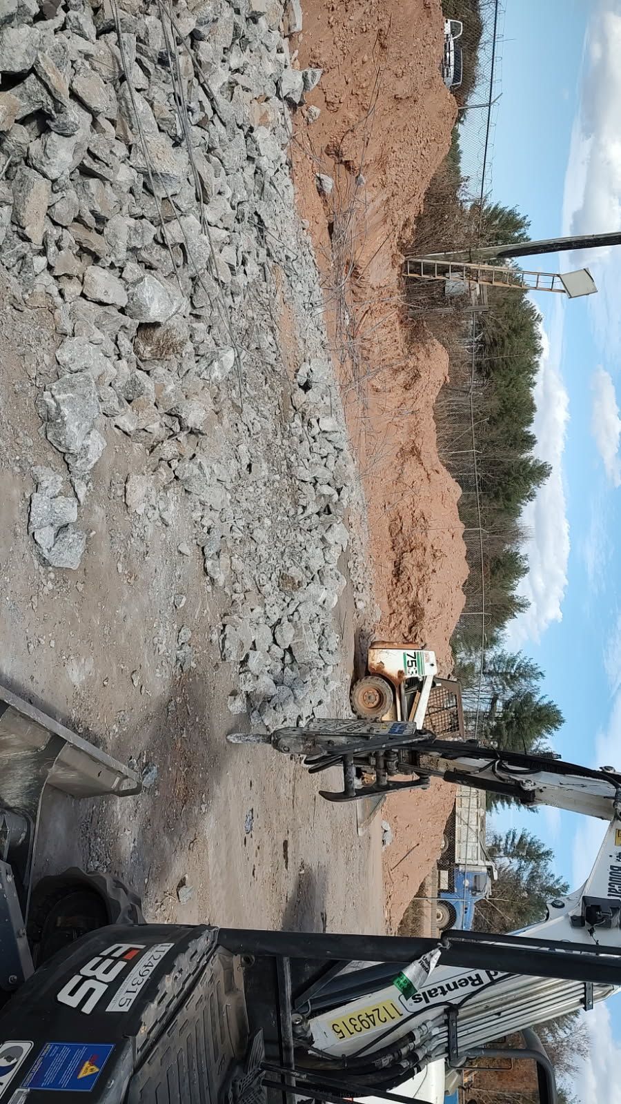Construction site with rubble, excavator arm, and dirt piles under a cloudy sky