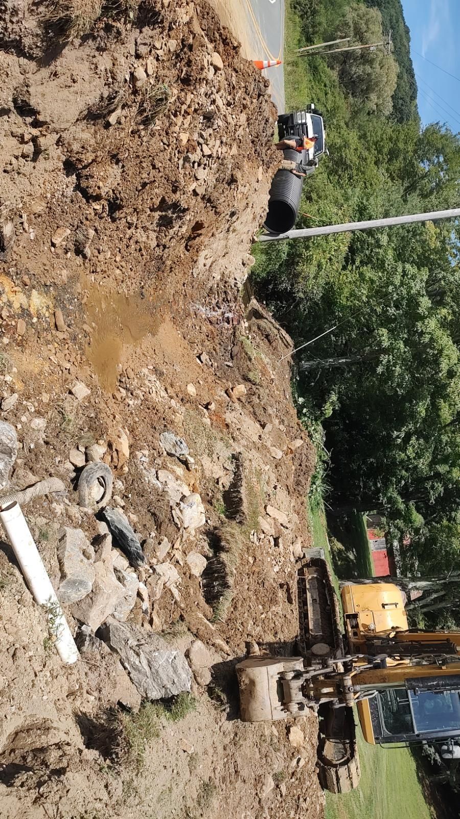 Construction equipment at a muddy landslide site with dirt piles and a partially visible excavator.