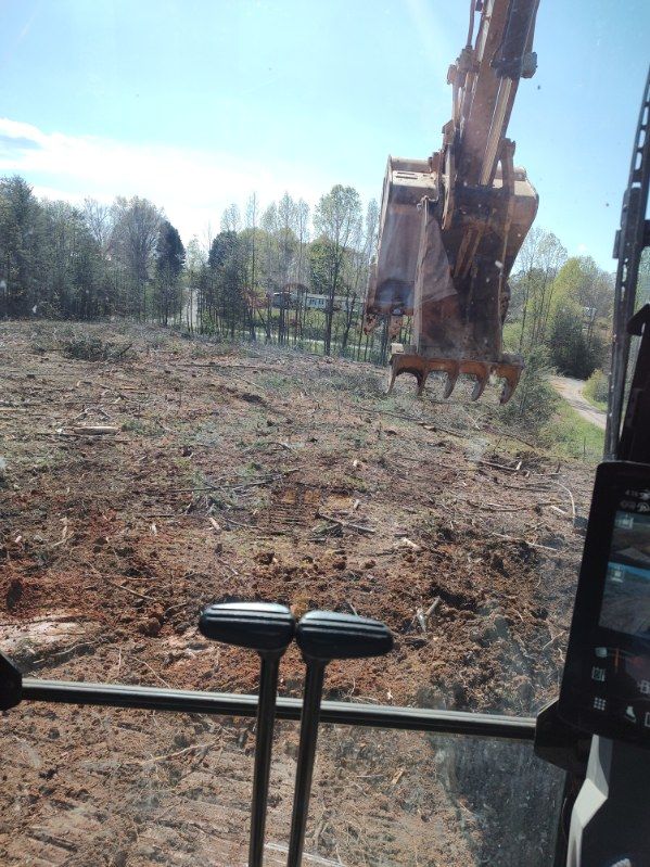 Excavator digging in a cleared field, viewed from inside a construction vehicle cab