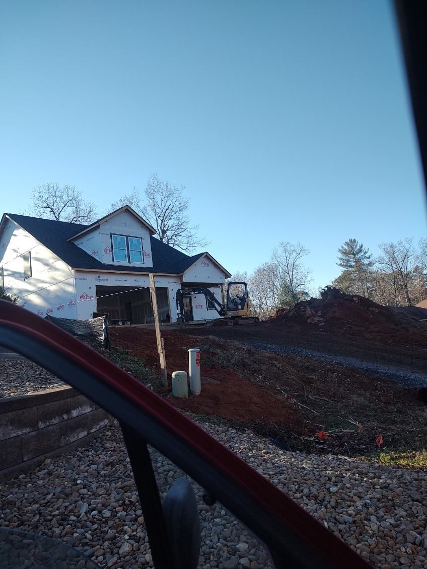 White house with porch on a sloped gravel lot, seen from inside a car at sunset.