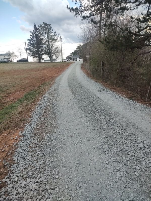 Gravel road curving through a rural landscape with bare trees and cloudy sky