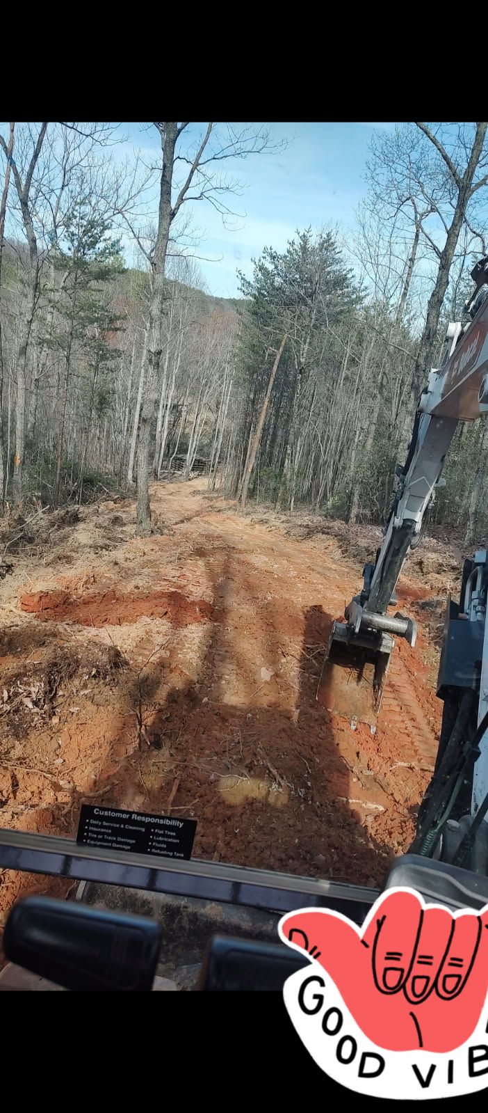 View from a construction vehicle driving on a muddy dirt road through a wooded area.
