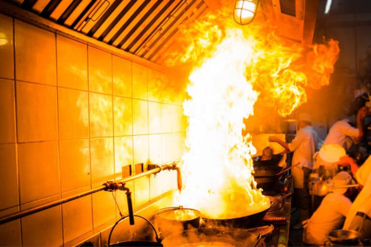 A large fire is coming out of a pot in a kitchen.